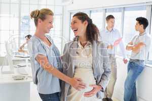 Casual businesswoman touching her pregnant colleagues belly