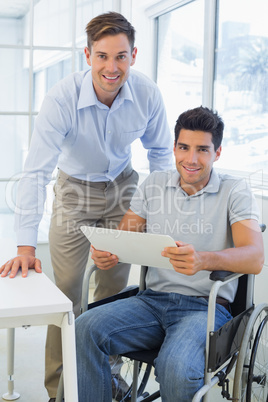 Casual businessman in wheelchair smiling at camera with colleagu