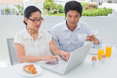 Smiling couple having breakfast together using laptop