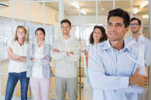 Casual boss smiling with arms crossed in front of business team