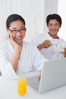 Couple in bathrobes spending the morning together using laptop