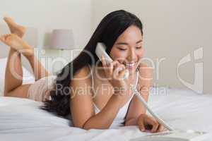 Happy woman lying on bed using land line phone