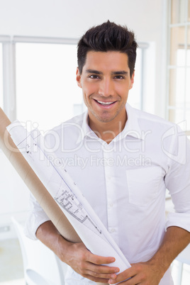 Casual handsome architect smiling at camera holding blueprint