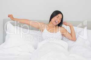 Smiling woman lying in bed stretching in the morning
