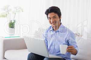 Happy man sitting on couch using laptop having coffee