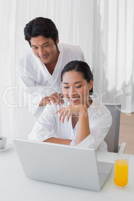 Couple in bathrobes using laptop together in the morning