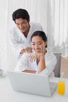 Couple in bathrobes using laptop together in the morning