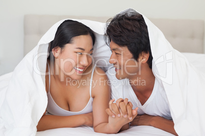 Happy couple lying on bed together under the duvet