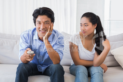Woman sitting on couch while boyfriend watches tv