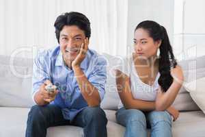 Woman sitting on couch while boyfriend watches tv