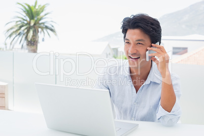 Smiling man using his laptop and talking on phone