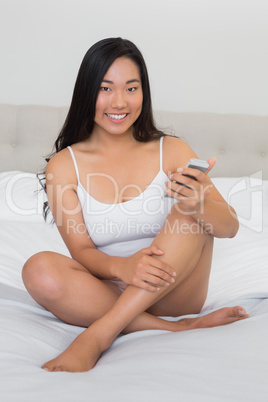 Happy woman sitting on bed holding smartphone