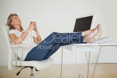 Casual businesswoman having a coffee with her feet up at desk