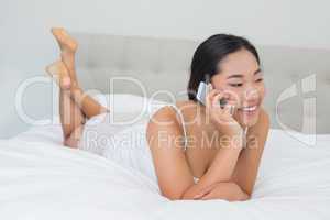 Smiling asian woman lying on bed talking on phone