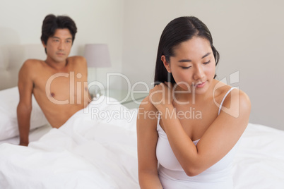 Boyfriend looking at girlfriend sitting on end of bed