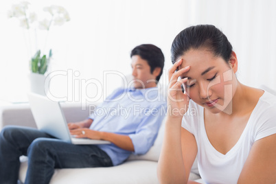 Upset woman sitting on couch while boyfriend uses laptop