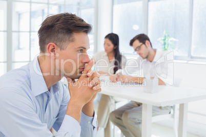 Casual businessman thinking with team behind him