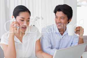 Couple using laptop with woman talking on phone