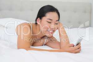 Smiling asian woman lying on bed sending a text