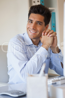 Casual businessman smiling at camera at his desk