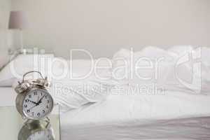 Messy bed with alarm clock on bedside table