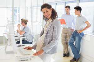 Pregnant businesswoman smiling at camera with team behind her