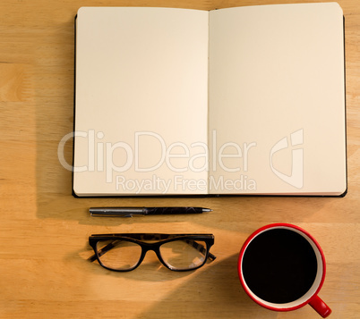 Overhead of open notebook with pen glasses and coffee