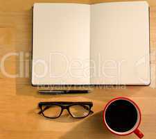 Overhead of open notebook with pen glasses and coffee