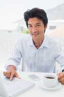 Smiling man having coffee and using laptop