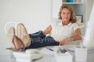 Casual businesswoman sitting at her desk with feet up