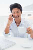 Smiling man having coffee and talking on phone