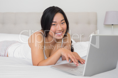 Happy woman lying on bed using laptop