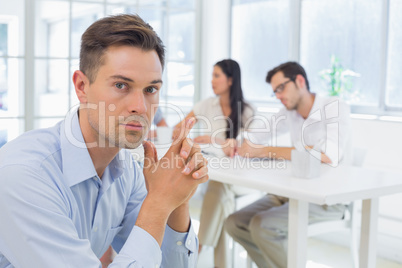 Casual businessman frowing at camera with team behind him