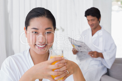 Woman in bathrobe having orange juice with boyfriend in backgrou