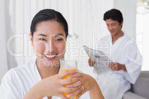 Woman in bathrobe having orange juice with boyfriend in backgrou