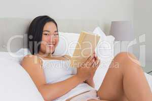 Smiling woman lying on bed reading
