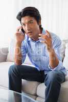 Annoyed man sitting on couch talking on phone