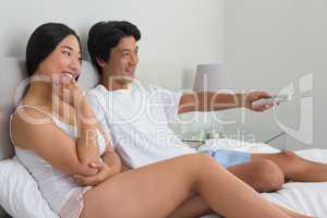 Smiling asian couple lying on bed watching tv