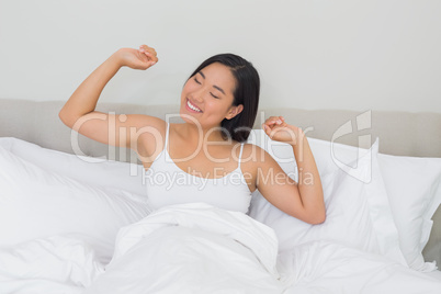 Smiling woman lying in bed stretching in the morning