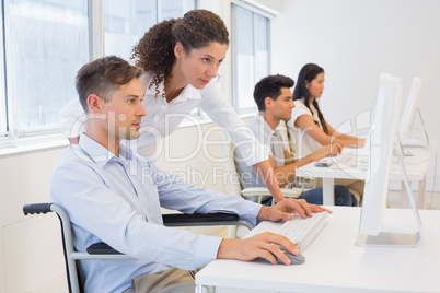 Casual businessman in wheelchair working at his desk with collea