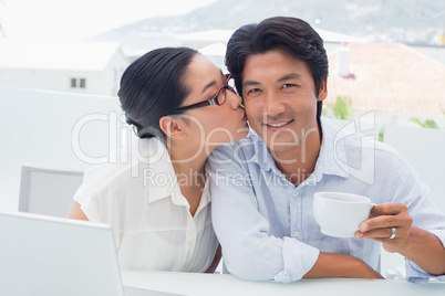 Woman kissing her boyfriend on the cheek having coffee