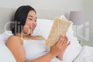 Smiling woman lying on bed reading