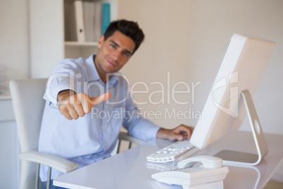Casual businessman giving thumbs up to camera at his desk