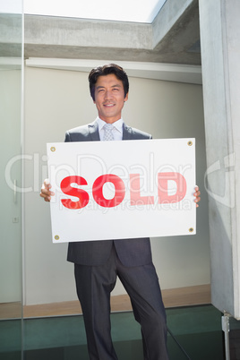 Confident estate agent standing at front door showing sold sign