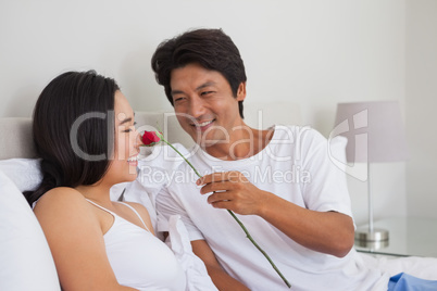 Man offering a red rose to girlfriend on bed