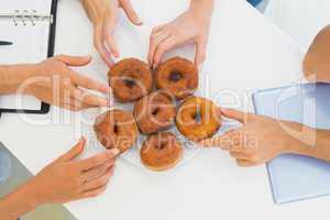 Business team reaching for doughnuts on table