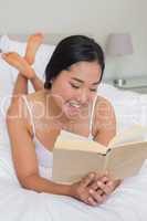 Smiling woman lying on bed reading