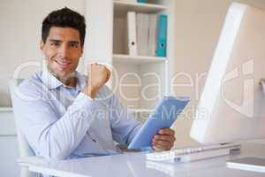 Casual businessman holding his tablet at his desk