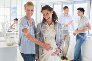 Casual businesswoman touching her pregnant colleagues belly