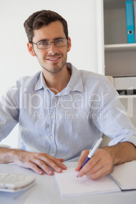 Casual smiling businessman taking notes at his desk